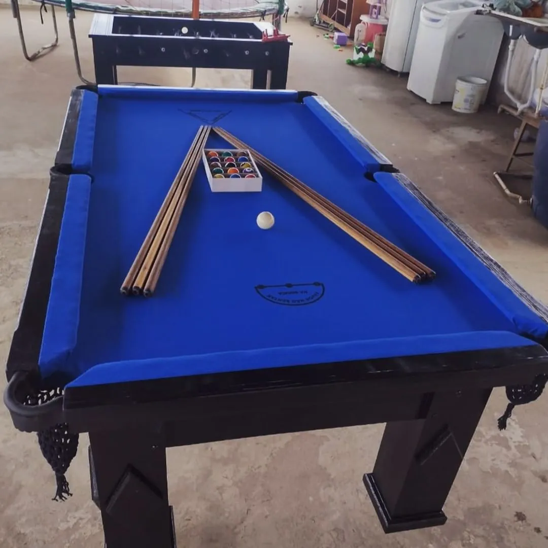 Mesa de sinuca de cestinha preta com tecido azul e tacos sobre a mesa